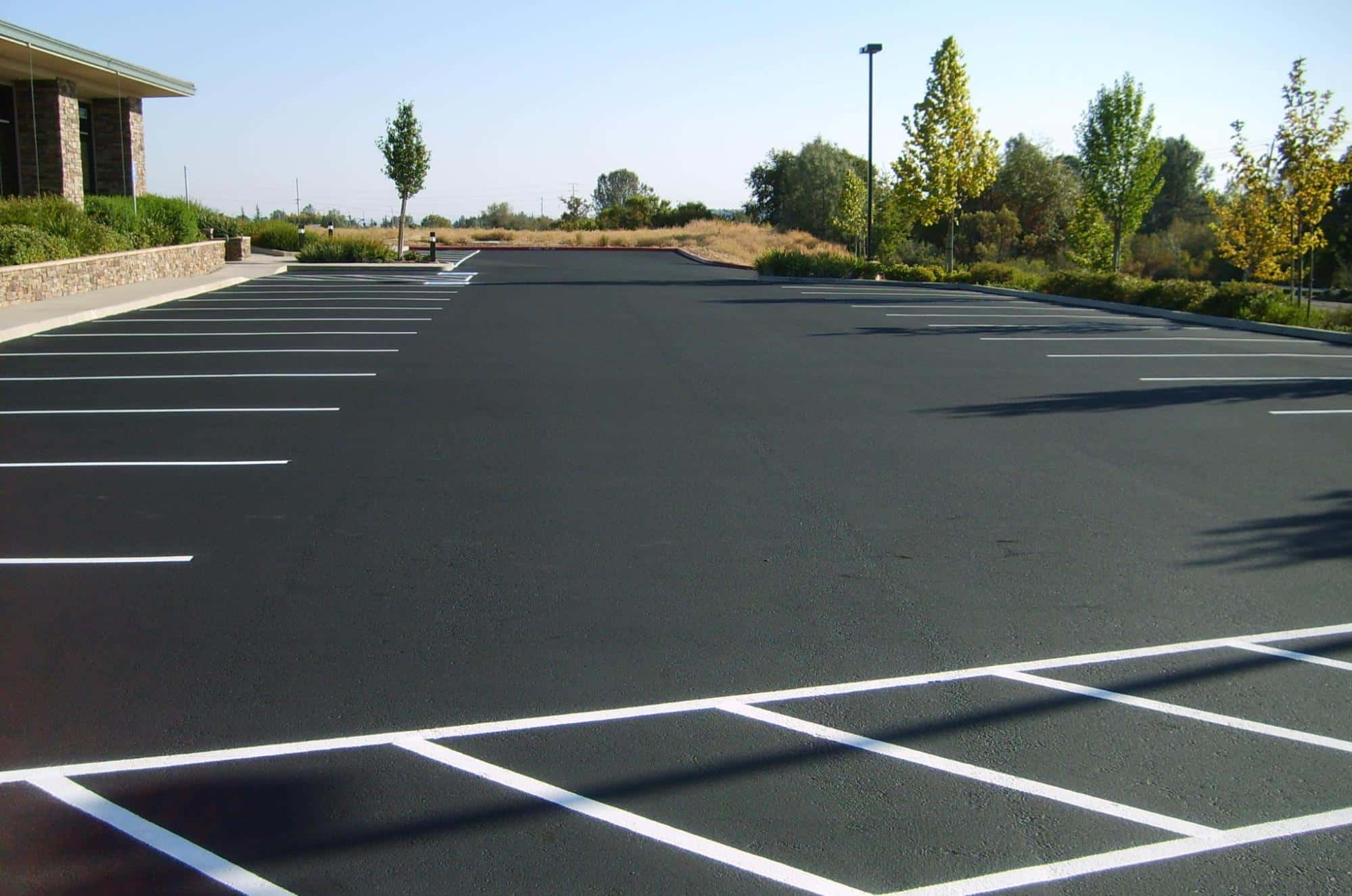 Freshly sealcoated commercial parking lot featuring bright white striping lines Freshly sealcoated commercial parking lot featuring bright white striping lines