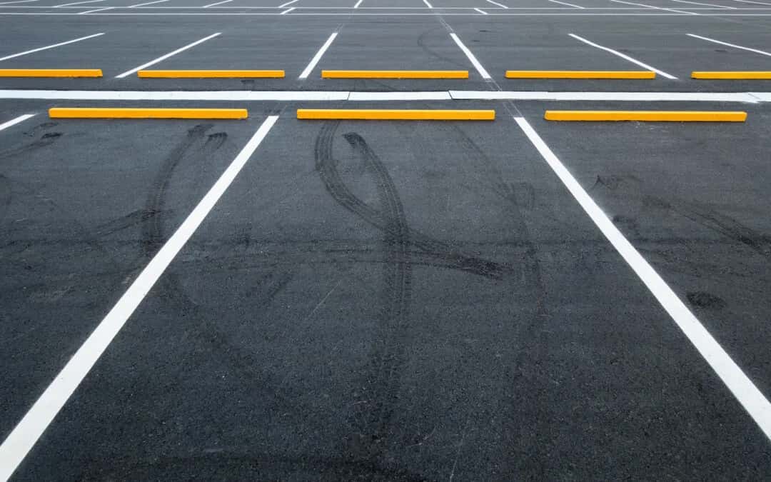 Freshly painted white parking stall lines and yellow wheel stops on dark asphalt Freshly painted white parking stall lines and yellow wheel stops on dark asphalt