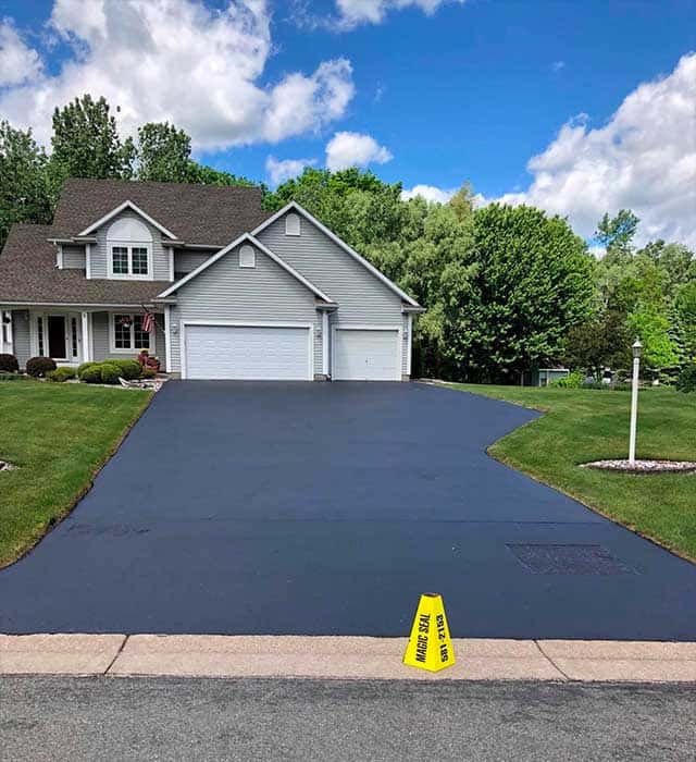 Freshly sealcoated asphalt driveway in front of a suburban residential home Freshly sealcoated asphalt driveway in front of a suburban residential home