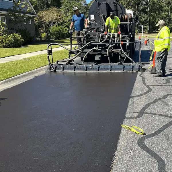 Paving crew using a truck-mounted spray bar unit to apply black asphalt sealcoat Paving crew using a truck-mounted spray bar unit to apply black asphalt sealcoat