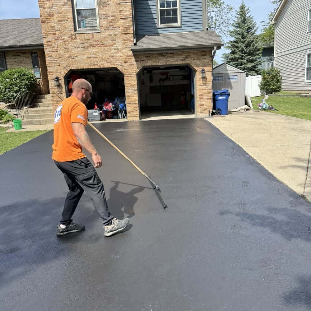 Worker manually spreading black asphalt sealcoat coating using a squeegee on a residential driveway Worker manually spreading black asphalt sealcoat coating using a squeegee on a residential driveway