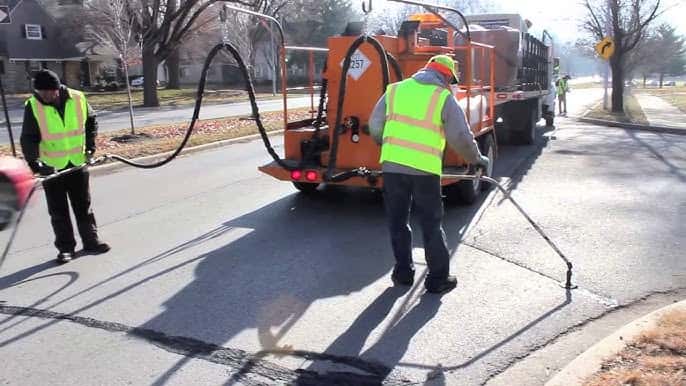 Paving crew applying hot asphalt crack sealant along street pavement with applicator wands Paving crew applying hot asphalt crack sealant along street pavement with applicator wands