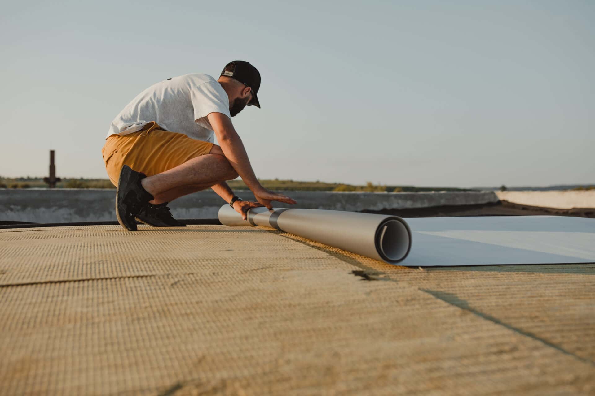 Roofer unrolling a white single-ply TPO membrane over insulation boards on a flat roof Roofer unrolling a white single-ply TPO membrane over insulation boards on a flat roof