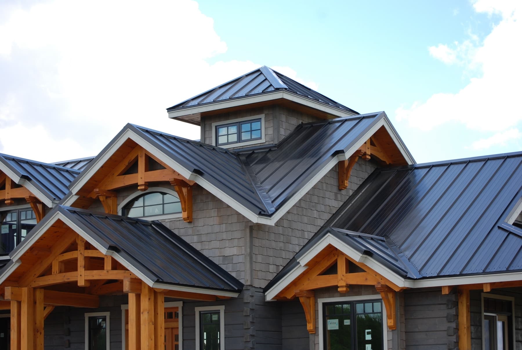 Craftsman-style home featuring exposed timber beams and a dark standing seam metal roof against a bright sky Craftsman-style home featuring exposed timber beams and a dark standing seam metal roof against a bright sky